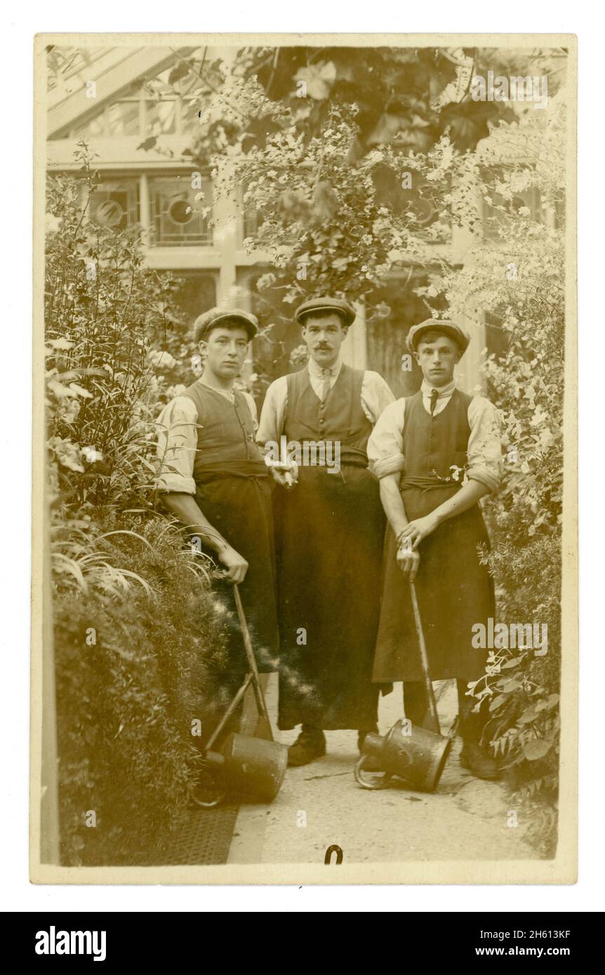 Original, clear early 1900's postcard of young Welsh gardeners next to a large house and conservatory. A poignant photograph of young men just before the outbreak of World War 1.  They are holding watering cans, and a brass sprayer pump, Lampeter area,  Ceredigion, Wales, U.K.  circa 1912 Stock Photo