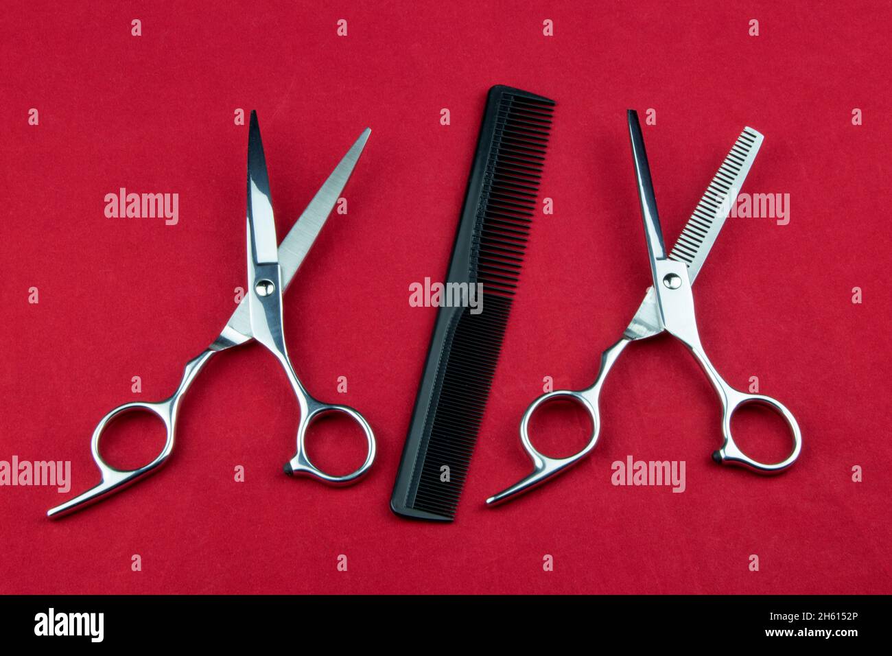 Hairdressing scissors and shears with comb on a red table surface Stock Photo