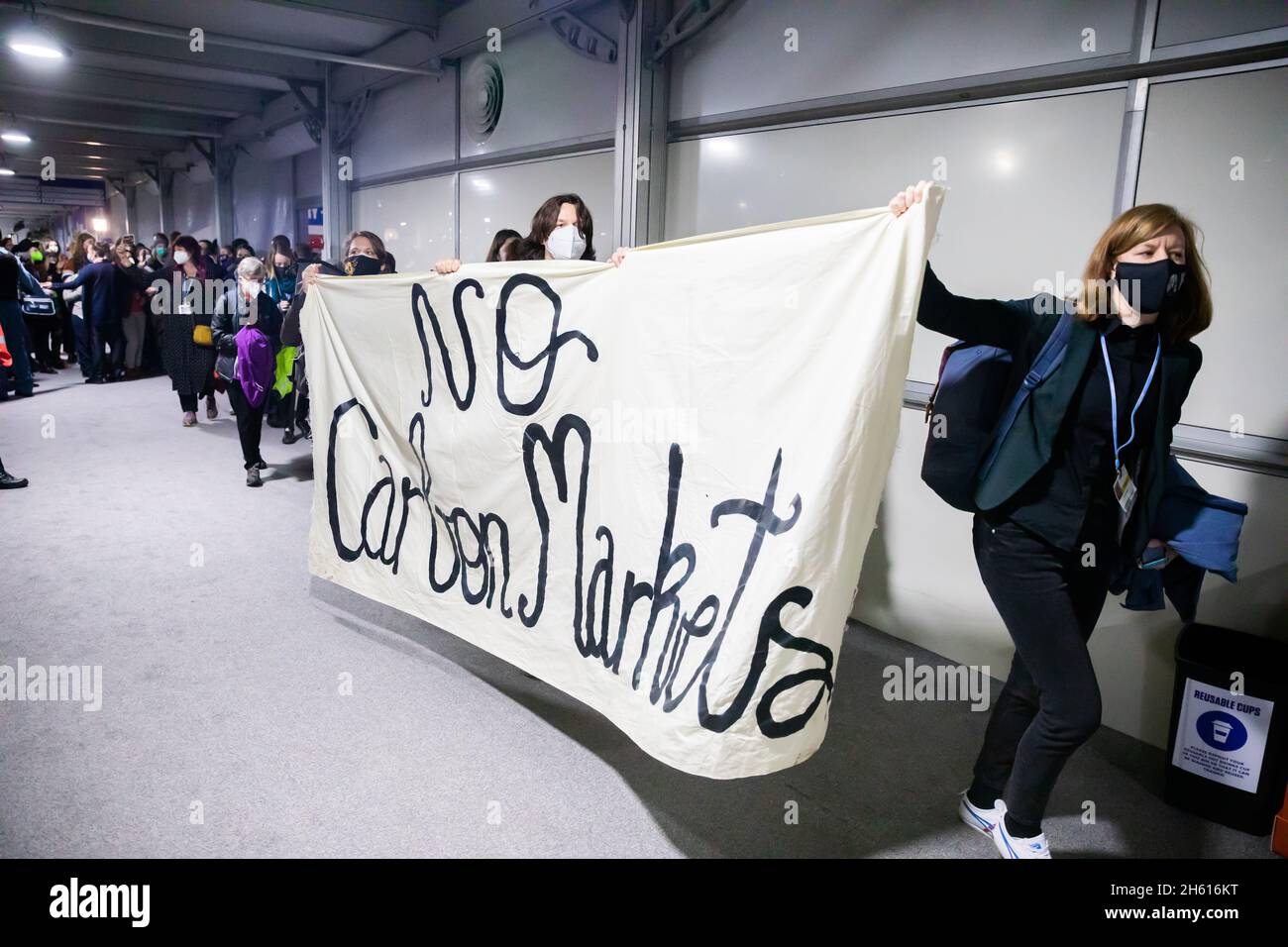 Glasgow, UK. 12th Nov, 2021. People march through a hall at the UN Climate Change Conference COP26 with a protest march for better climate protection. A banner reads "No Carbon Markets". For two weeks in Glasgow, around 200 countries are wrestling with how the goal of limiting global warming to 1.5 degrees compared to pre-industrial times can still be achieved. Credit: Christoph Soeder/dpa/Alamy Live News Stock Photo