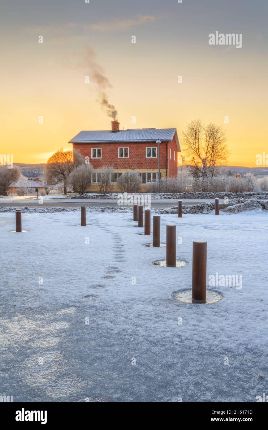 posts and house with smoke and snow during sunset Stock Photo