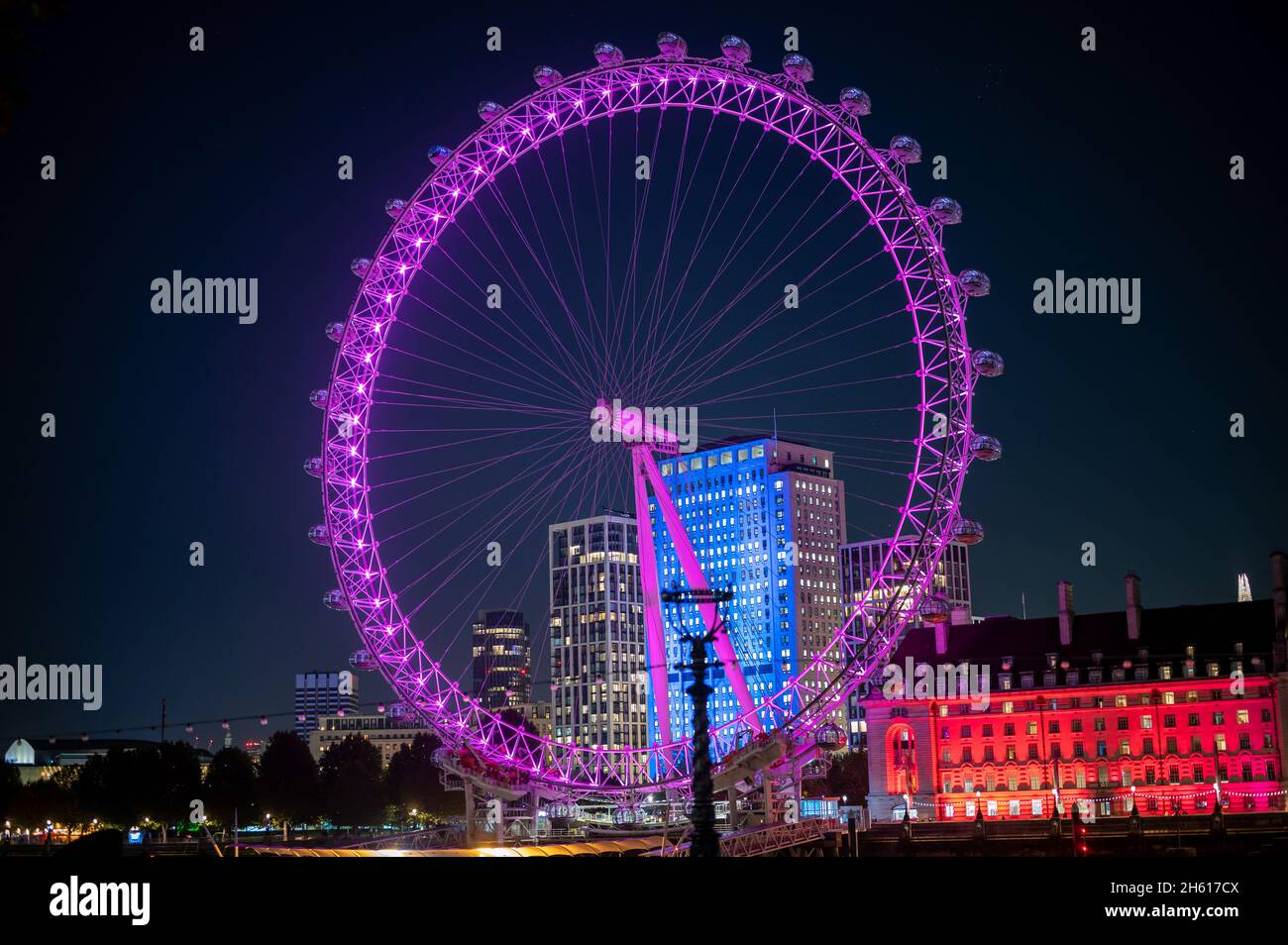 LONDON - NOVEMBER 1, 2021: Colourfully lit London Eye and part of County Hall at night Stock Photo
