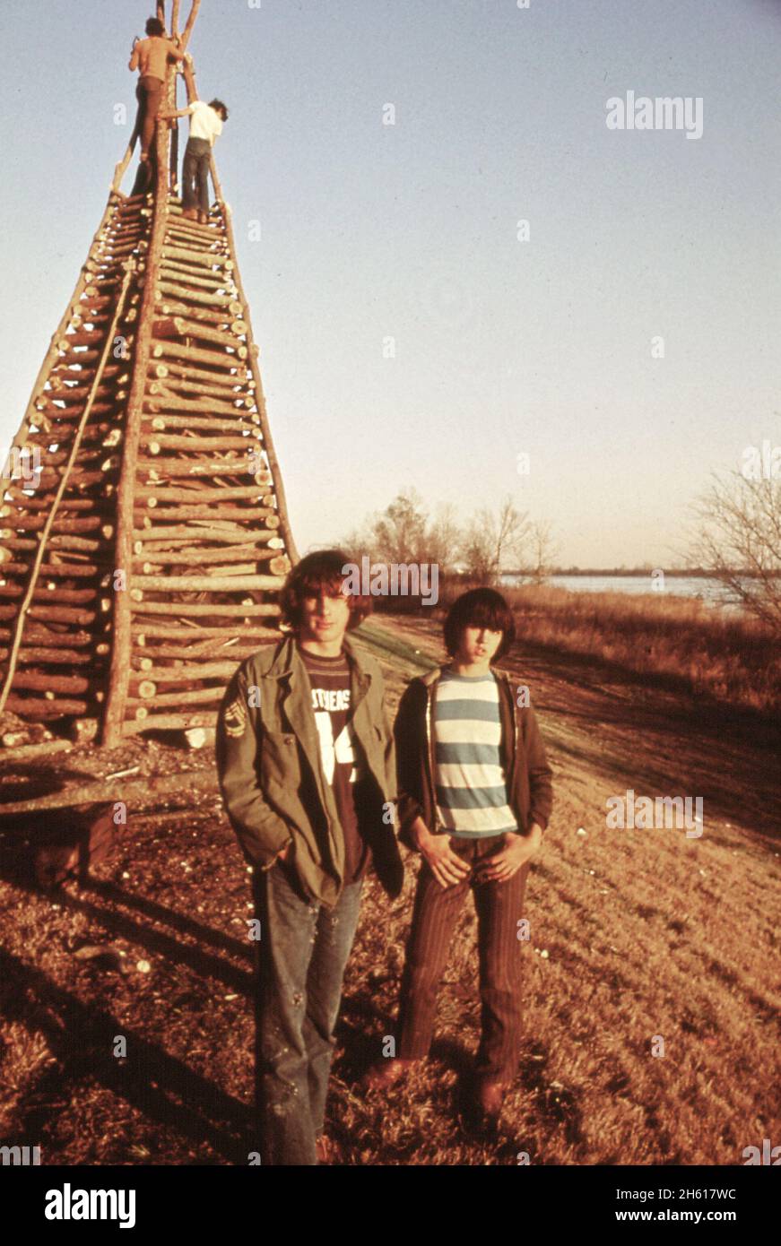 Kids stand in front of lumber stacked on Mississippi River levee for the traditional Christmas Eve bonfire ca. December 1972 Stock Photo