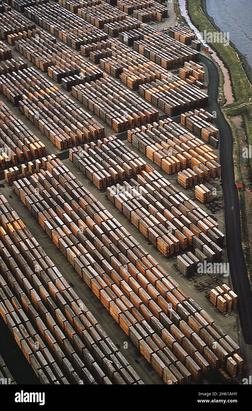 1970s America Lumber stacked in a lumber yard near a river in