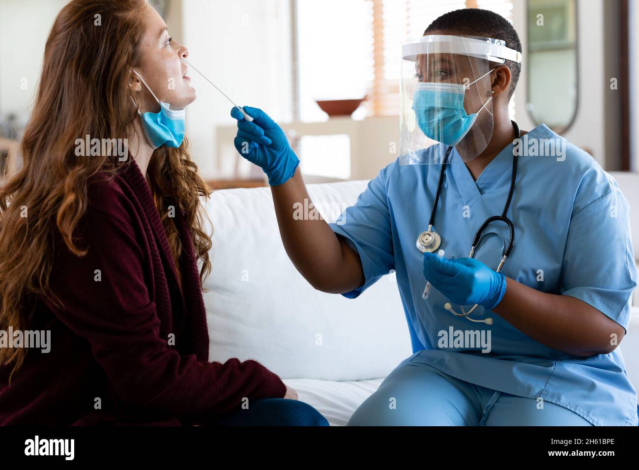 Female doctor in protective face mask taking swab test of woman in clinic during coronavirus crisis Stock Photo