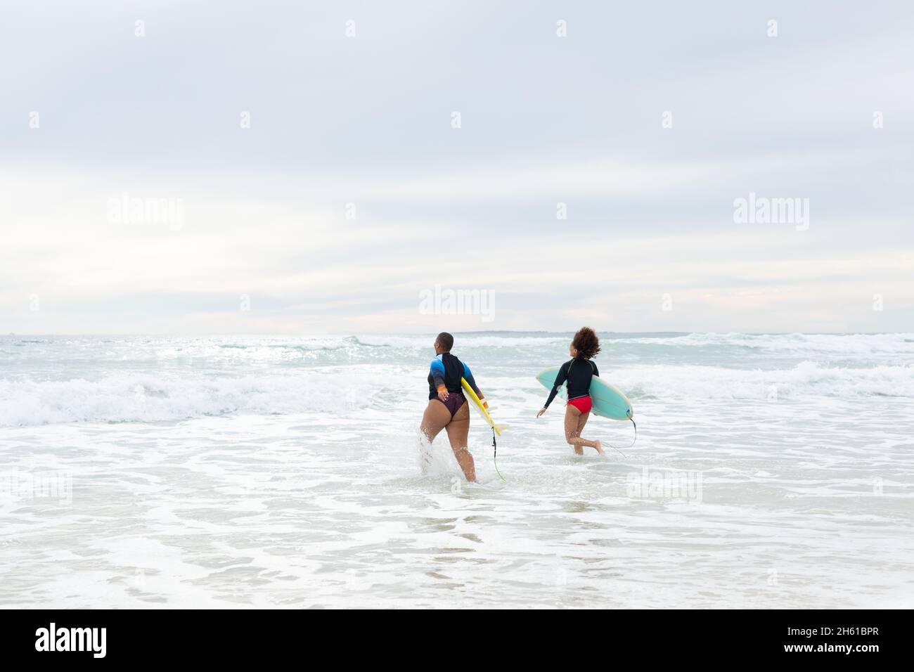 Carefree multiracial female friends with surfboards running in sea against sky during weekend Stock Photo