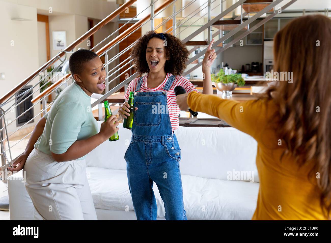 Cheerful multiracial female friends singing and having fun while holding beer bottles at home Stock Photo