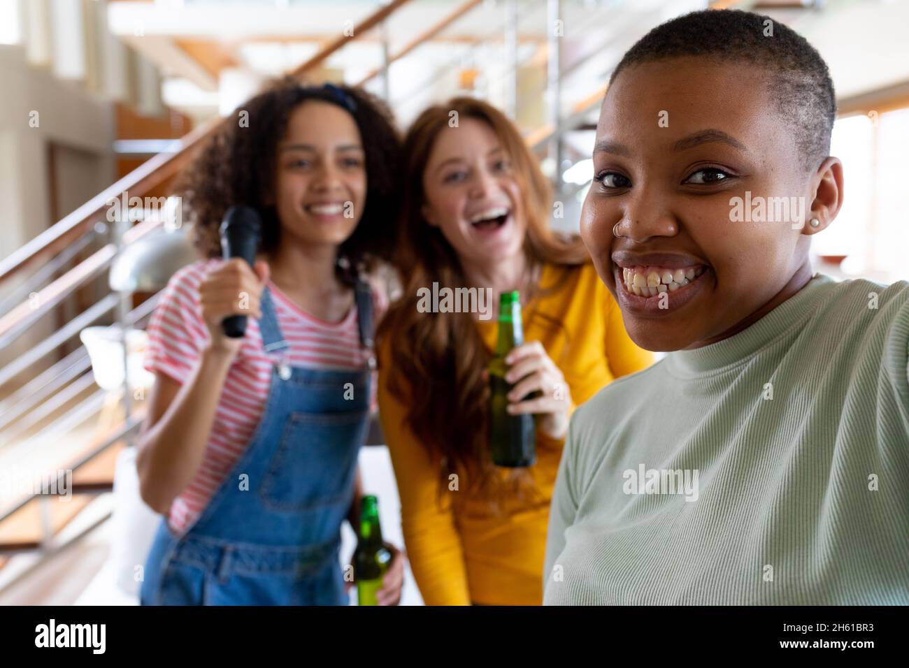 Happy woman taking selfie with multiracial female friends holding beer bottles at home Stock Photo