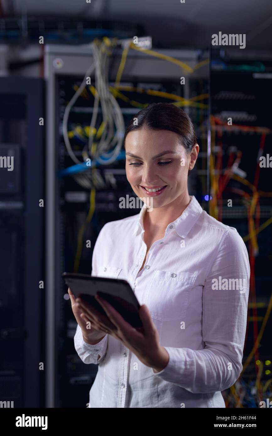 Caucasian female engineer smiling while using digital tablet in computer server room Stock Photo