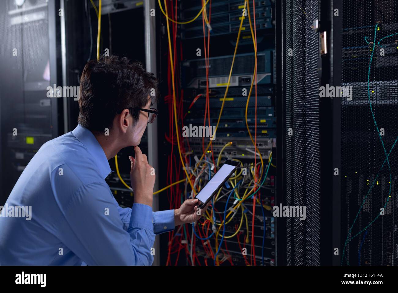 Thoughtful asian male engineer using digital tablet and inspecting computer server in server room Stock Photo
