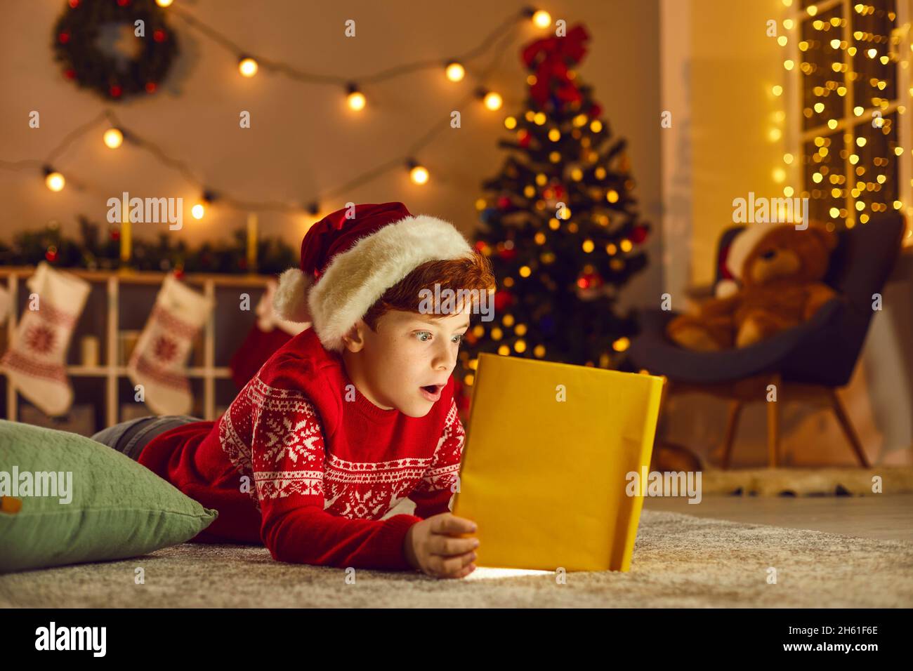 Little kid reading a book of wonderful stories and fairy tales on Christmas Eve at home Stock Photo