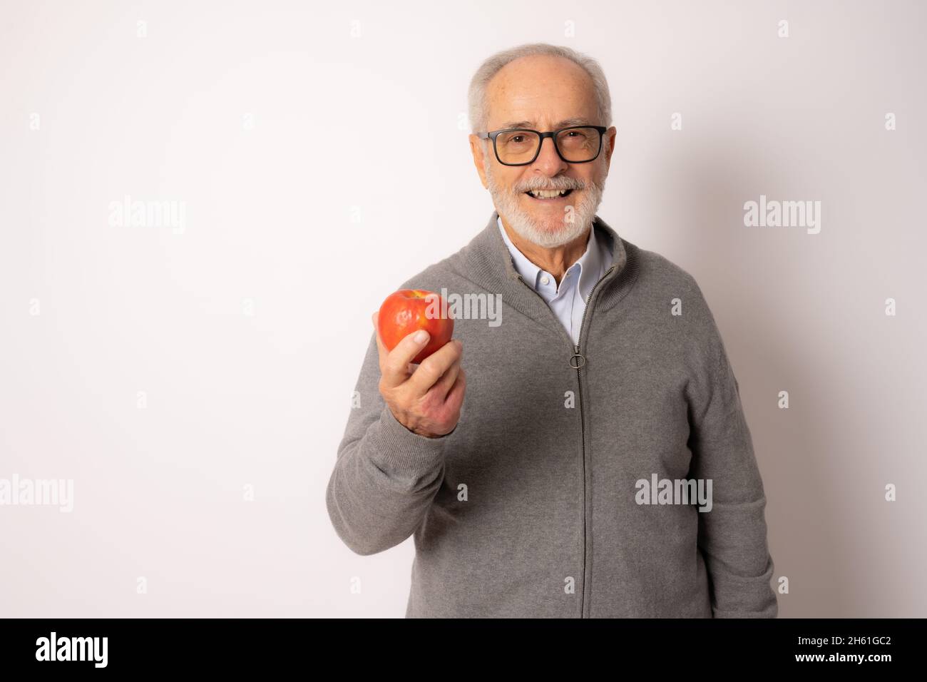 Senior happy man wearing casual sweater eating an apple isolated over white background. Stock Photo