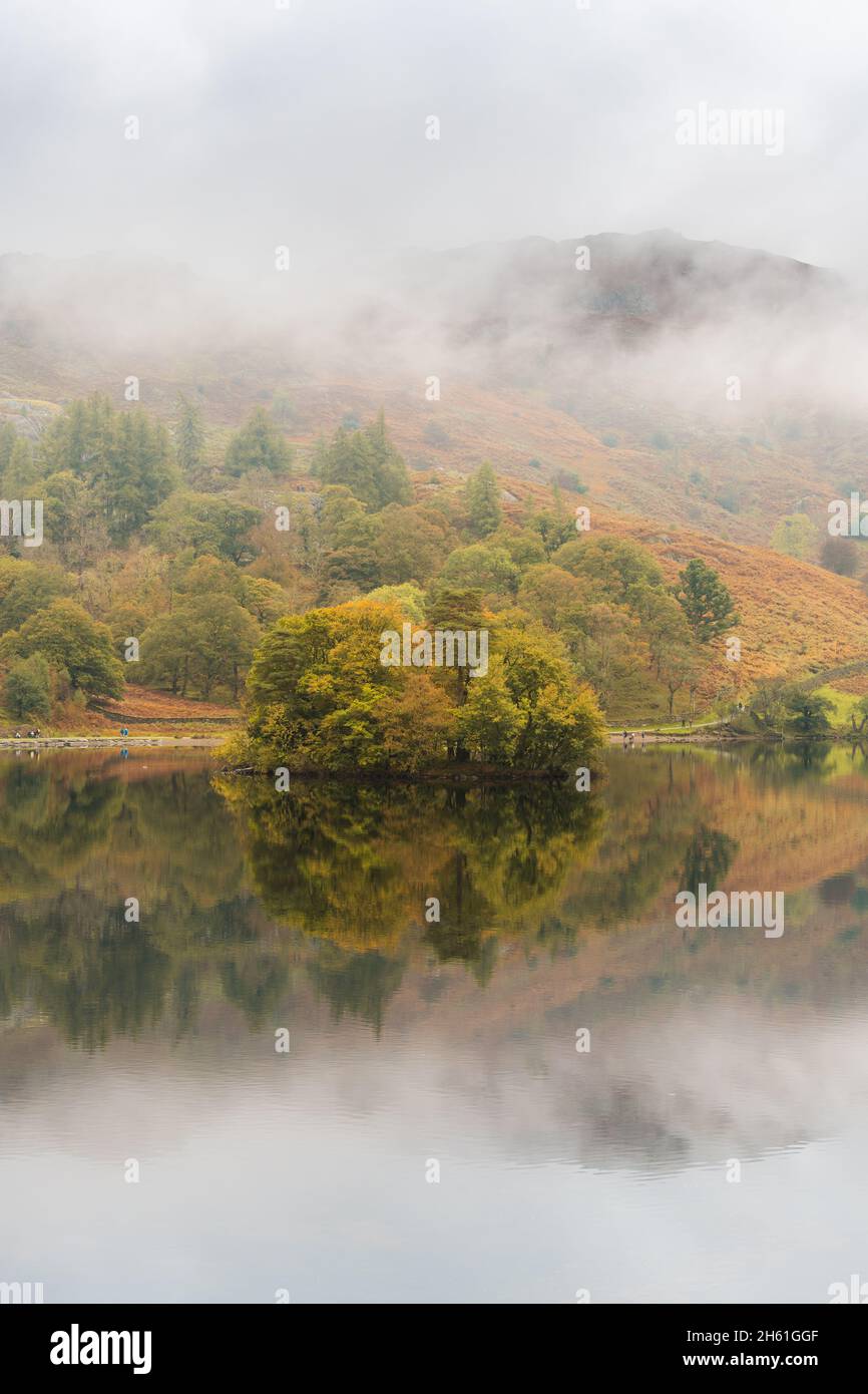 Looking across the misty calm vista towards heron island residing on the banks of Rydal Water in the Lake District, autumn just around the corner. Stock Photo