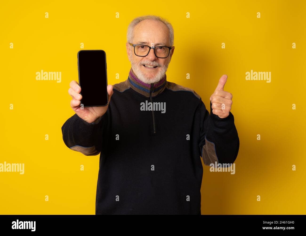 Lifestyle, technology and old people concept: Handsome old gray-haired man dressed in smart casual style using a smartphone and smiling over yellow ba Stock Photo