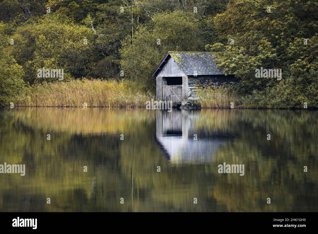 Looking across the calm vista towards the old boathouse which resides on the banks of Rydal Water in the Lake District, autumn just around the corner. Stock Photo