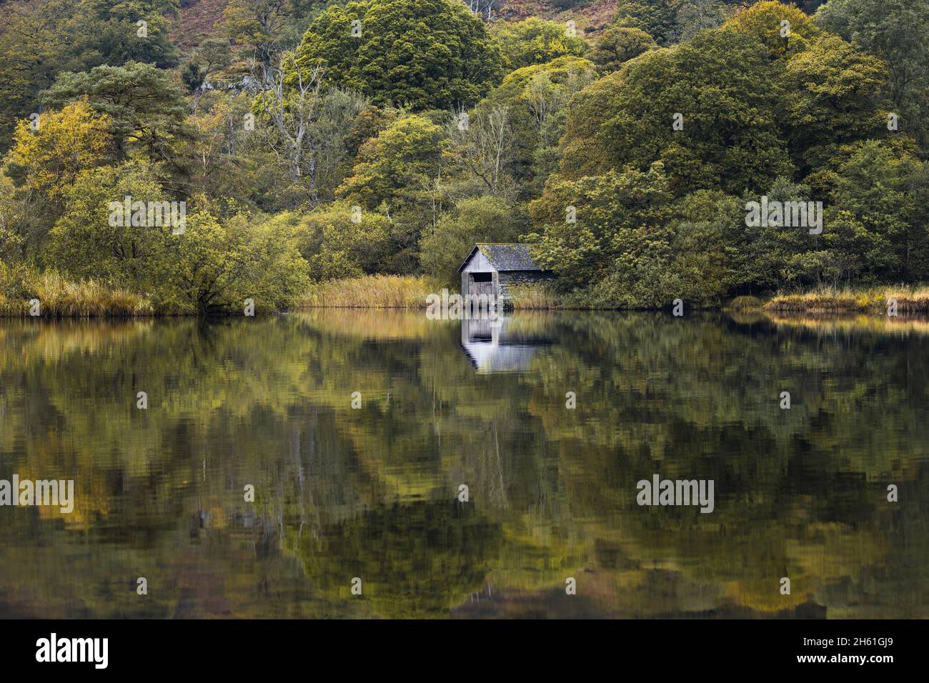 Looking across the calm vista towards the old boathouse which resides on the banks of Rydal Water in the Lake District, autumn just around the corner. Stock Photo