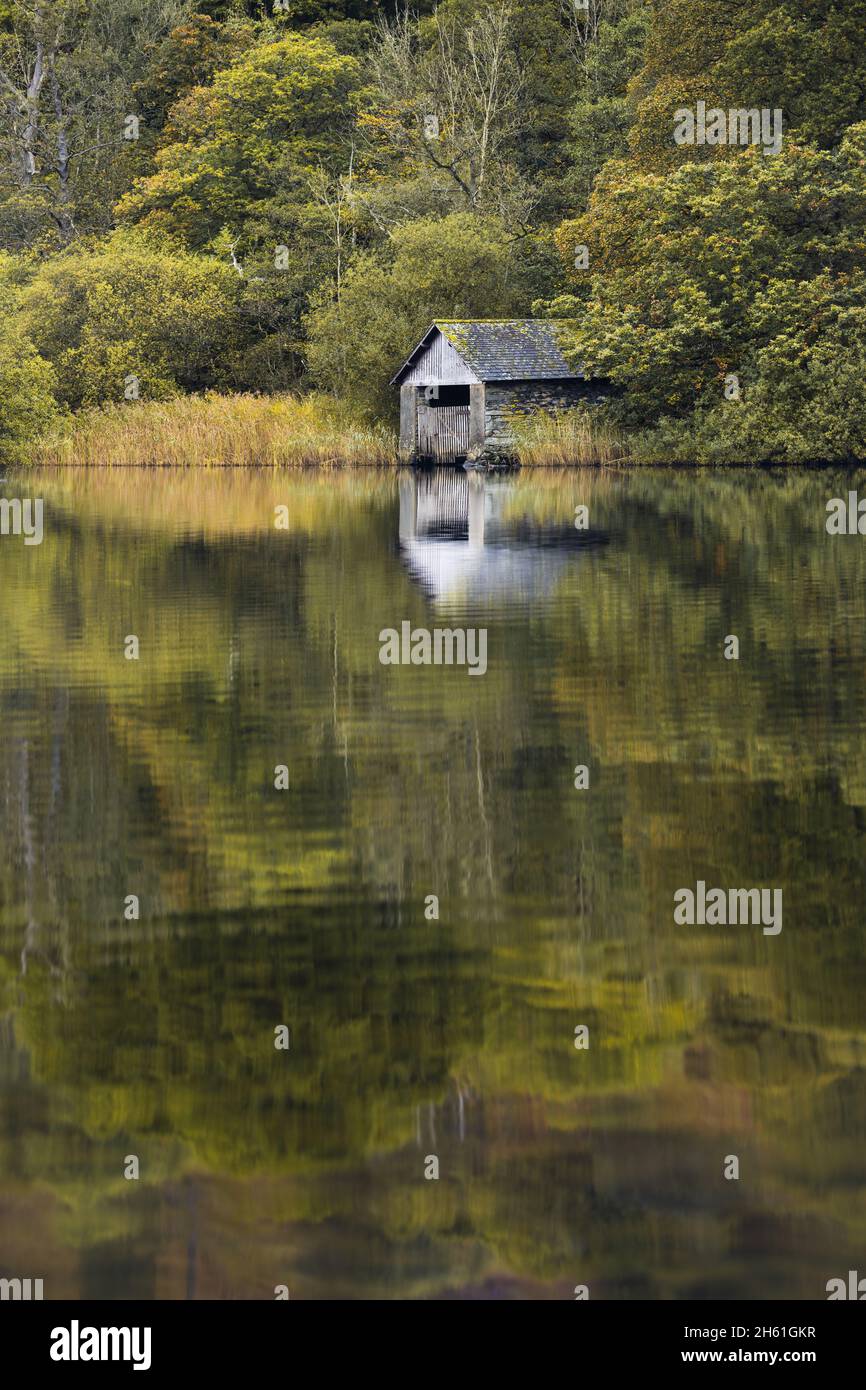 Looking across the calm vista towards the old boathouse which resides on the banks of Rydal Water in the Lake District, autumn just around the corner. Stock Photo