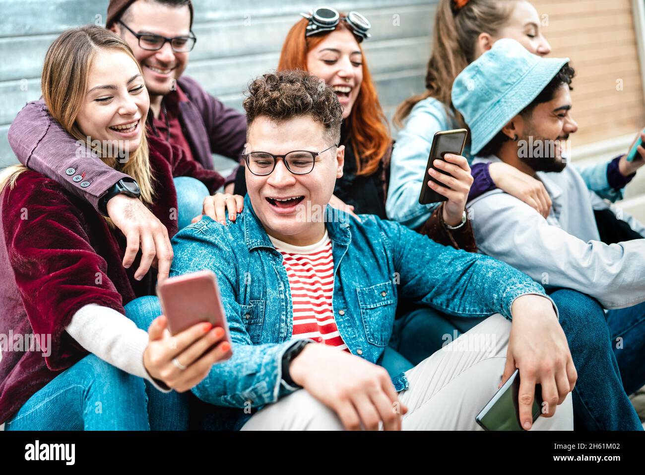 Young milenial friends having fun with mobile phone at campus college yard - Joyful men and women spending time together Stock Photo