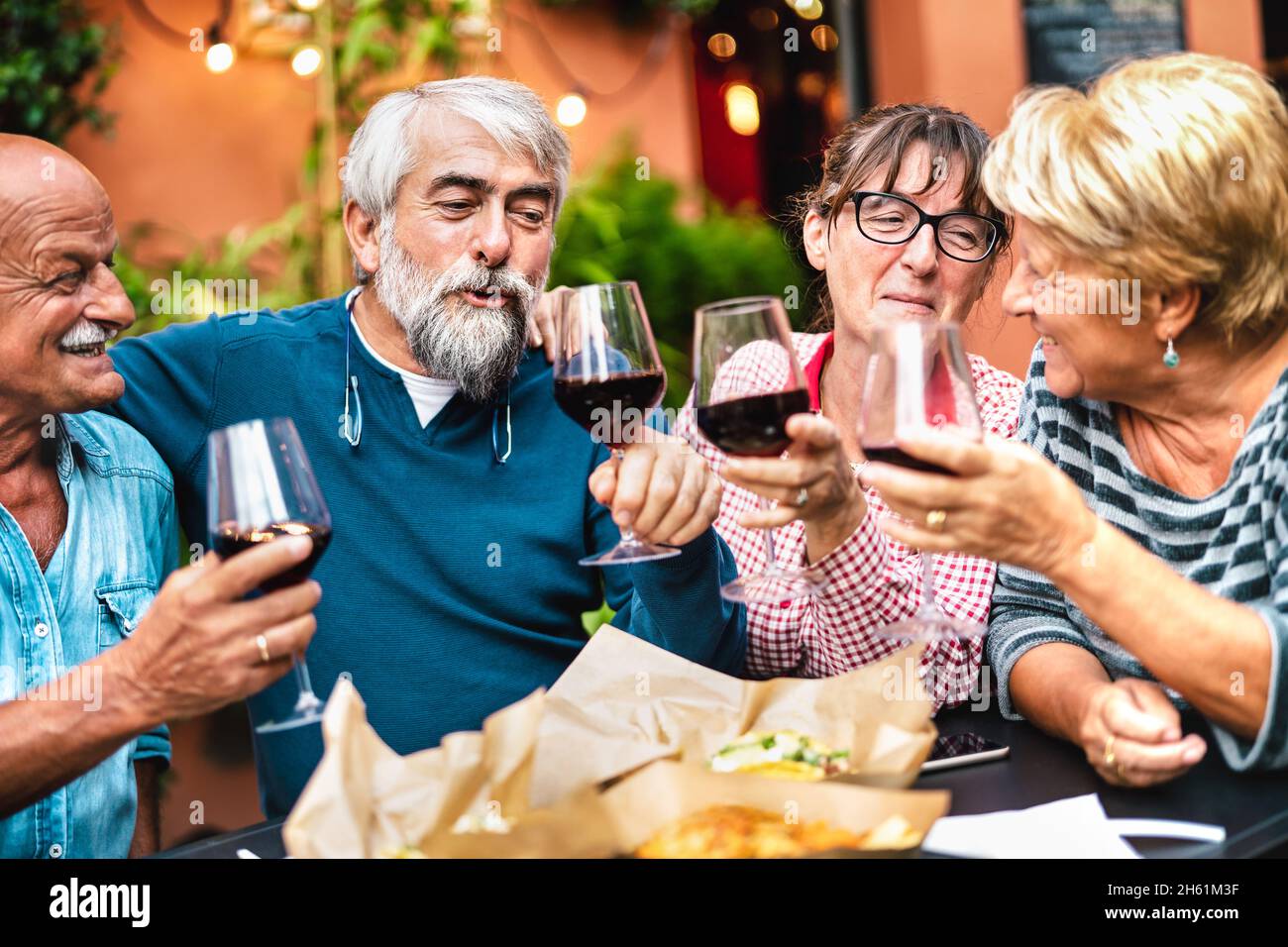 Happy seniors having fun toasting red wine at dinner garden party - Retired couples drinking at restaurant together - Dinning friendship concept Stock Photo