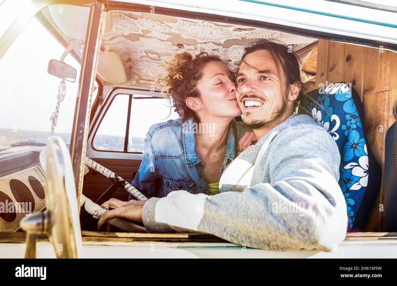 Hipster couple ready for roadtrip on oldtimer mini van transport - Travel lifetstyle concept with indie people kissing on minivan adventure trip Stock Photo