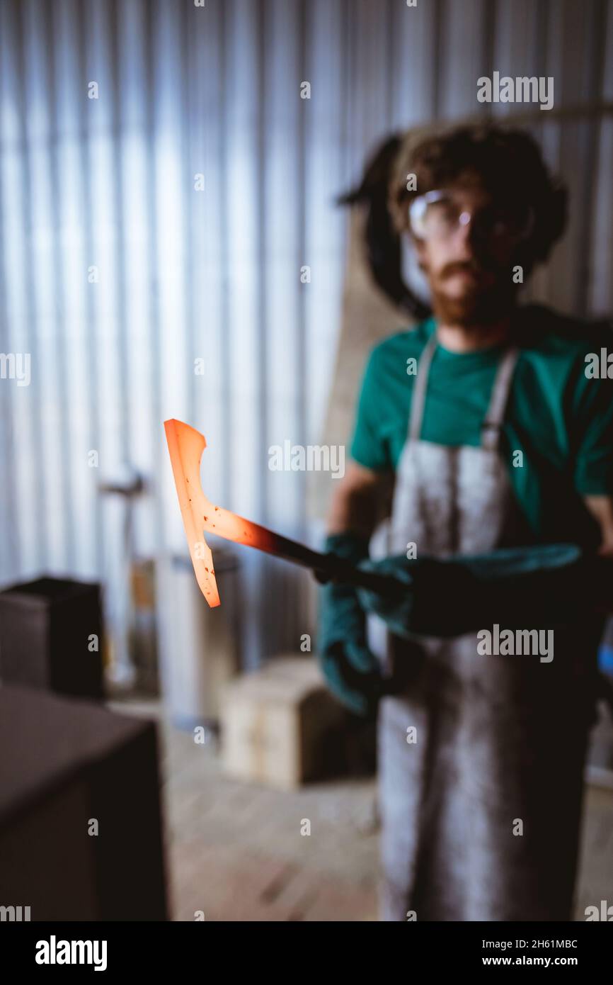 Blacksmith holding hot hammer shaped metal while working in manufacturing industry Stock Photo