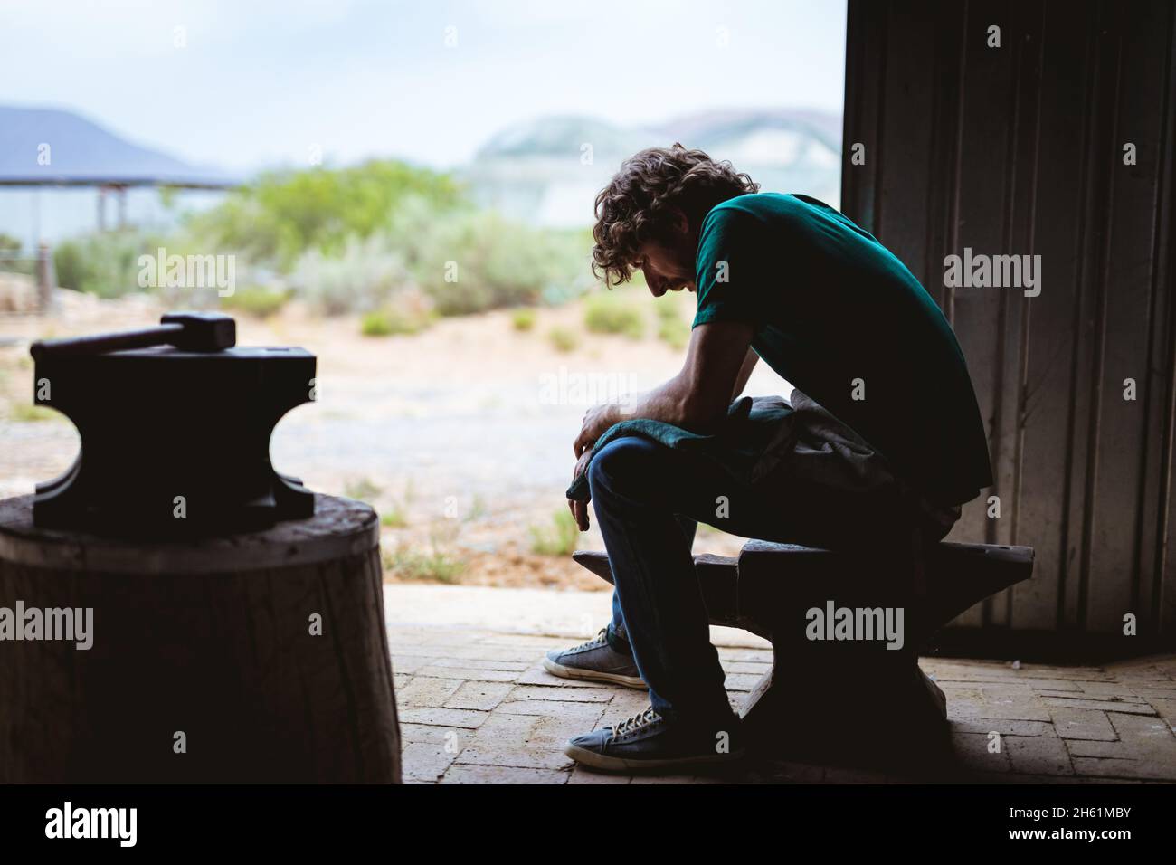 Side view of blacksmith sitting on anvil in metal industry Stock Photo