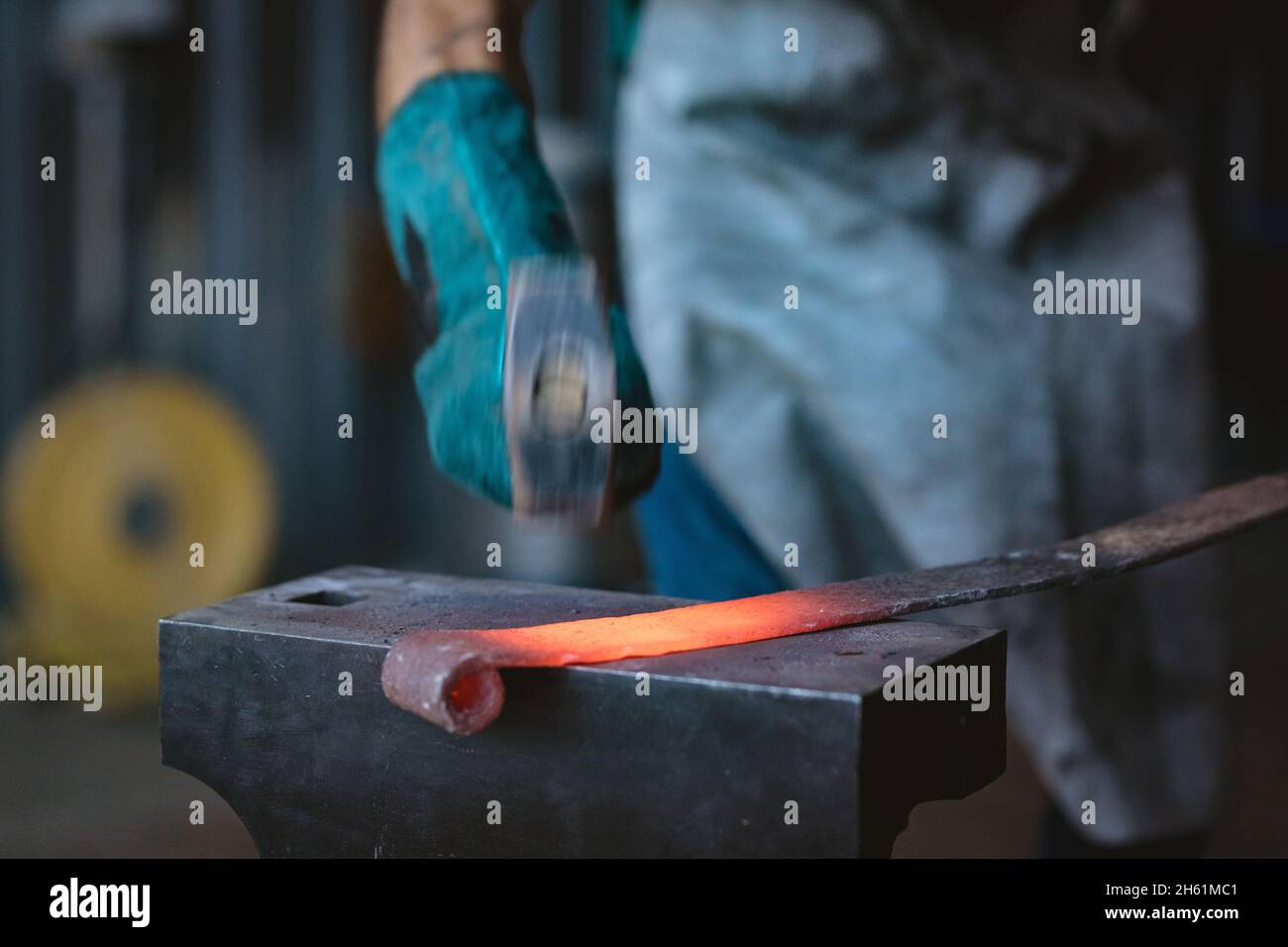 Cropped image of blacksmith in protective glove forging with hammer on anvil in industry Stock Photo