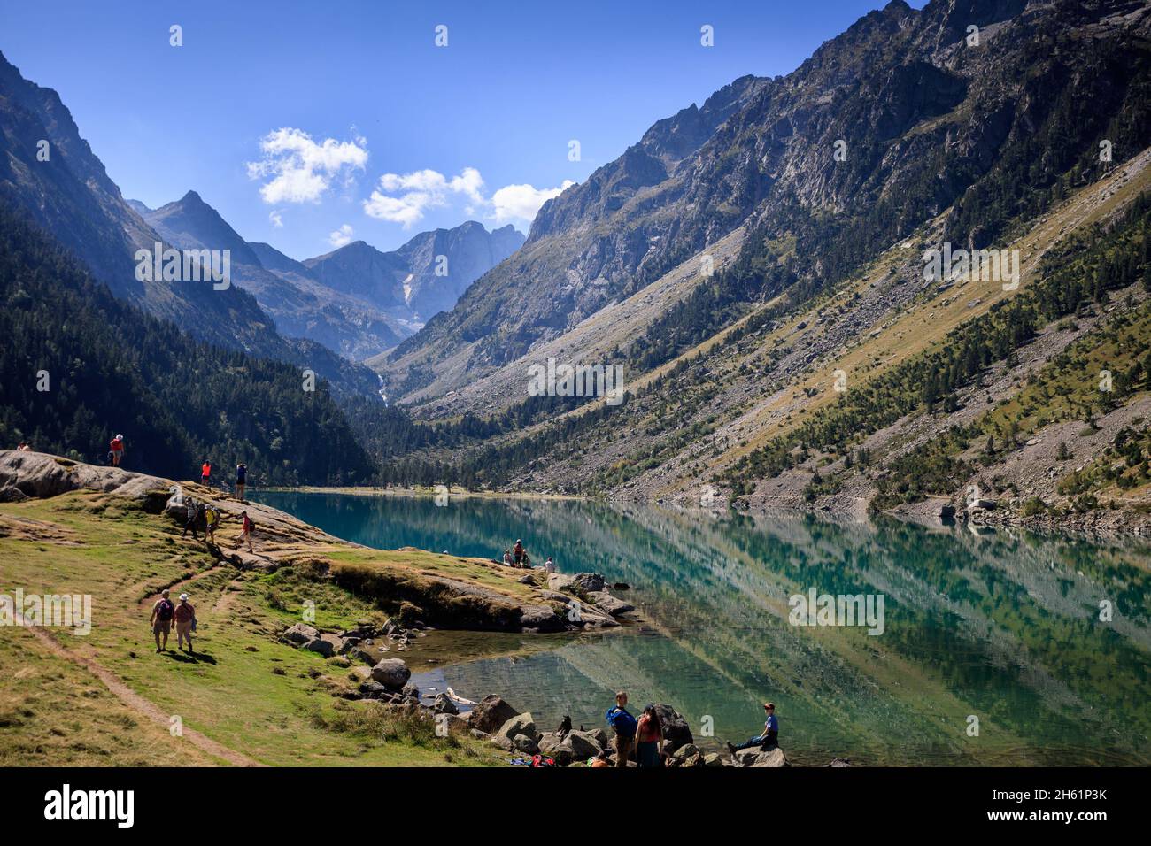 Hikers in the lake Gaube in Cauterets, the French Pyrenees. It is surrounded by the peaks Mayouret, Paloumeres and the Gaube. Stock Photo