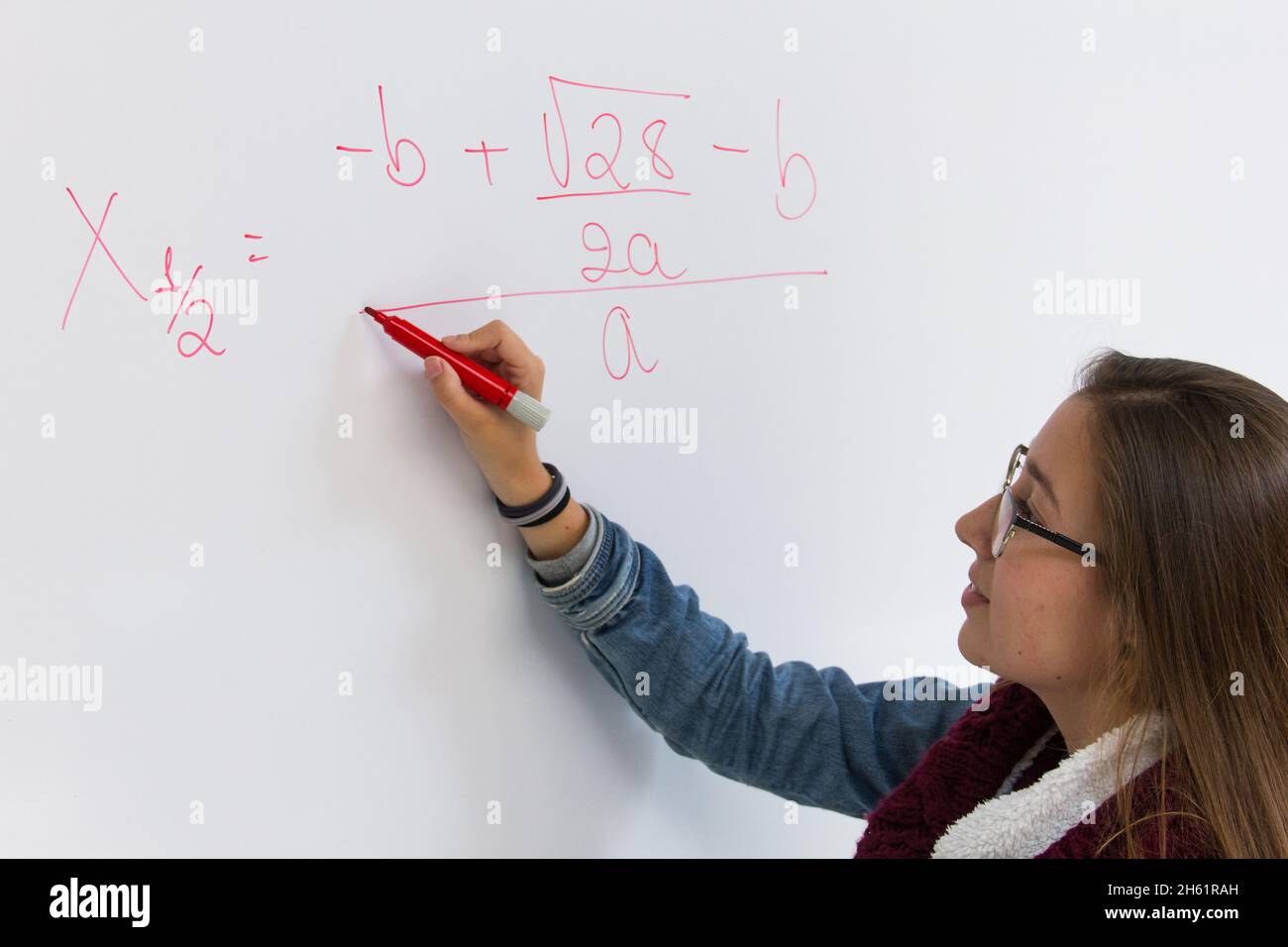 Bright student solving math equation. Blonde young girl writing with red pen on white board. Intelligent woman concept, teacher explaining problem Stock Photo