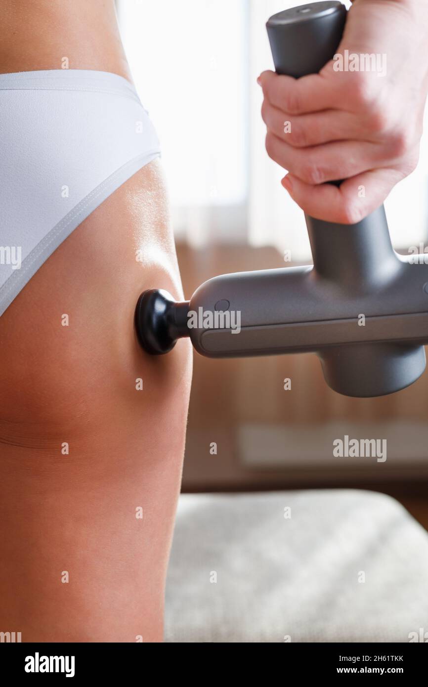 Self-massage of the female buttock with a percussion massage gun at home. Shock  massage to restore fascia muscles and trigger points Stock Photo - Alamy