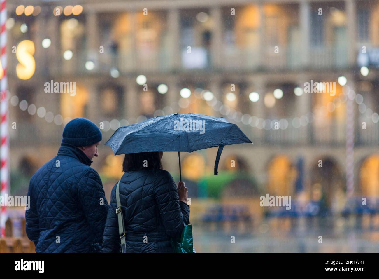 A couple carry an umbrella as they do their Christmas shopping in the Halifax Piece Hall , Calderdale , West Yorkshire. The bad weather and heavy rain didn't stop them. Stock Photo