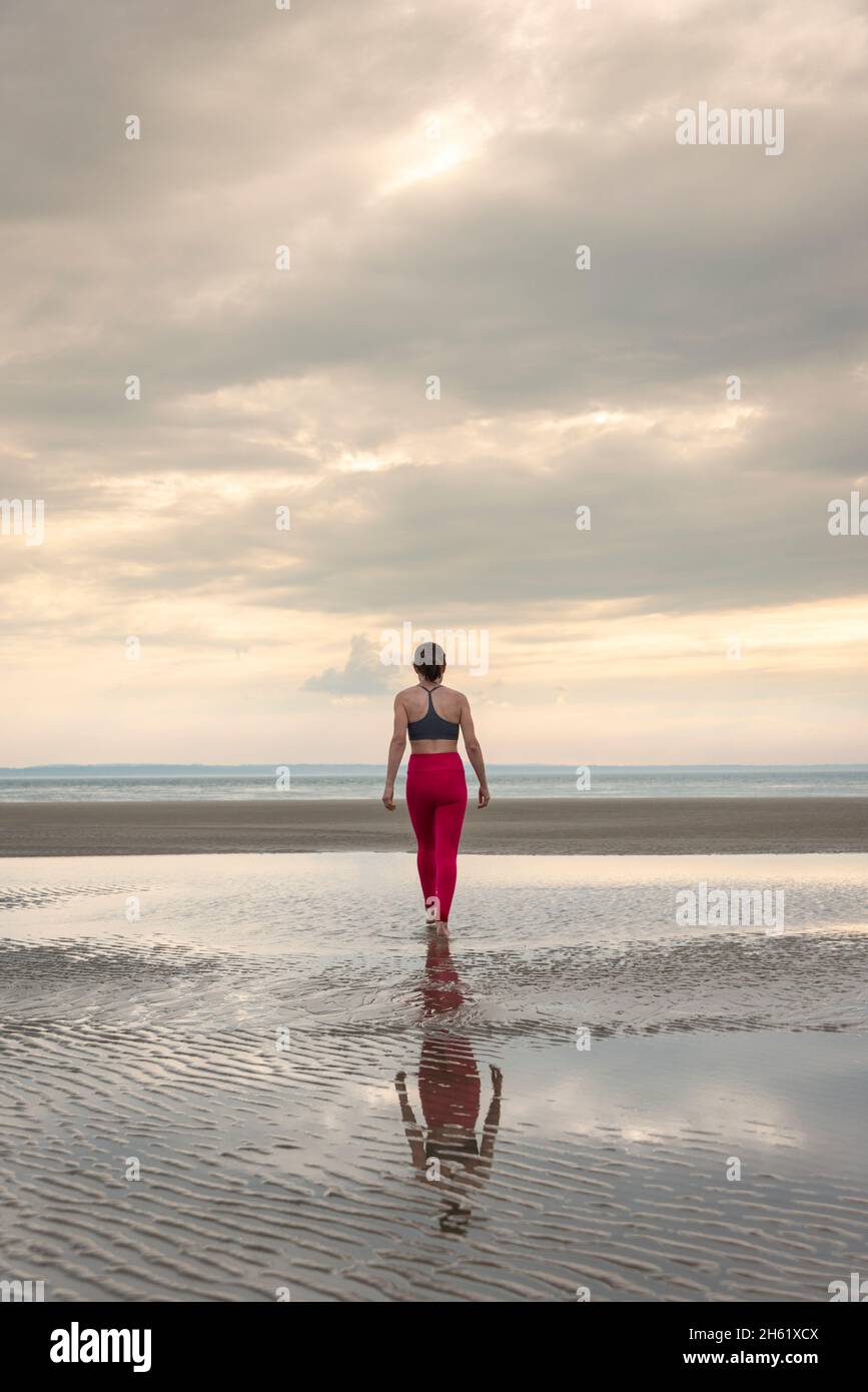 Woman walking on a beach in exercise clothes, rear view. Stock Photo