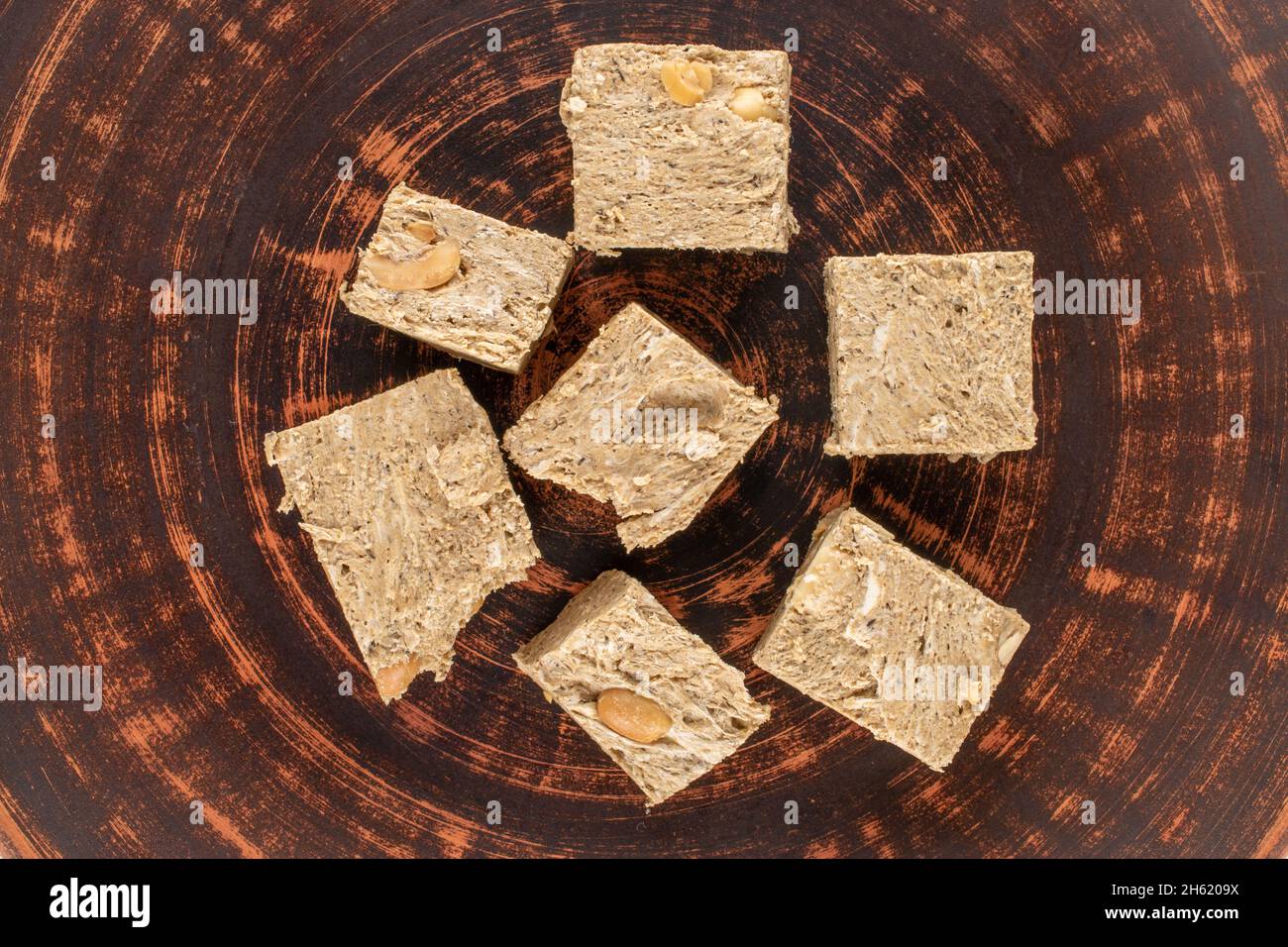 Several pieces of halva with peanuts on a clay dish, closeup, top view
