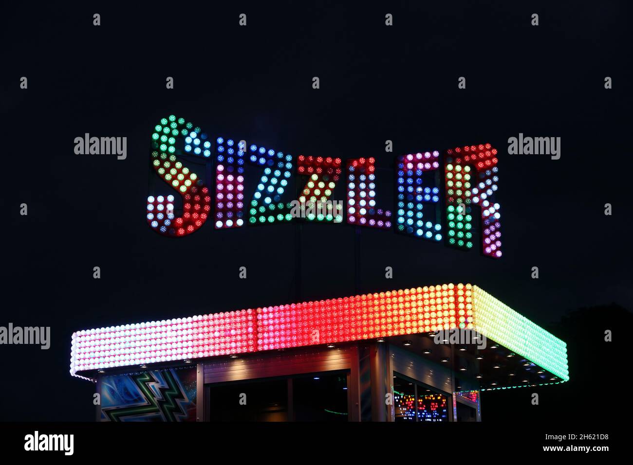 Illuminated Sizzler sign over fairground attraction, after dark at York Balloon Fiesta 2021 Stock Photo