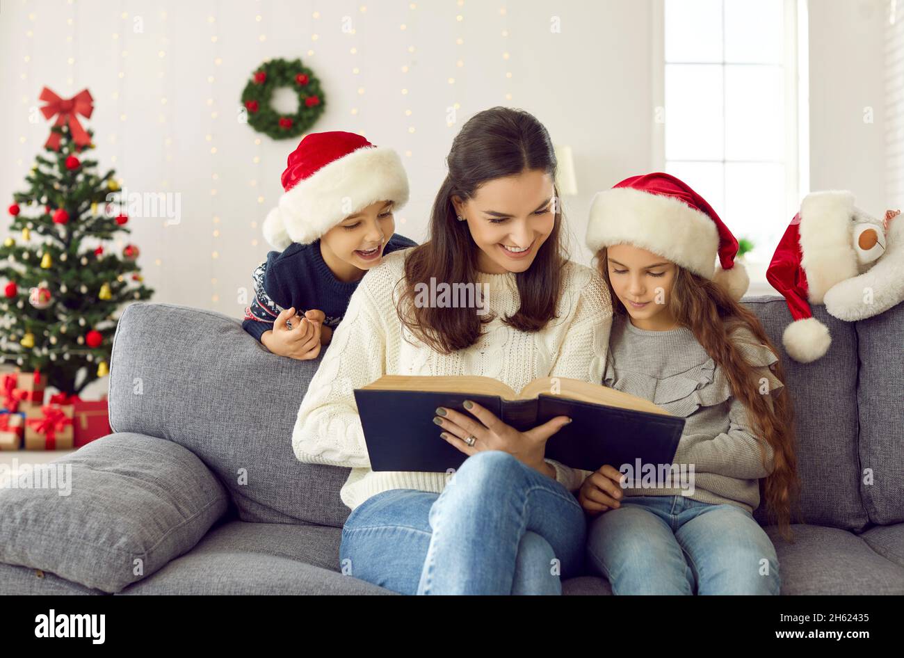 Happy family sitting on couch in decorated living room and reading book of Christmas stories Stock Photo