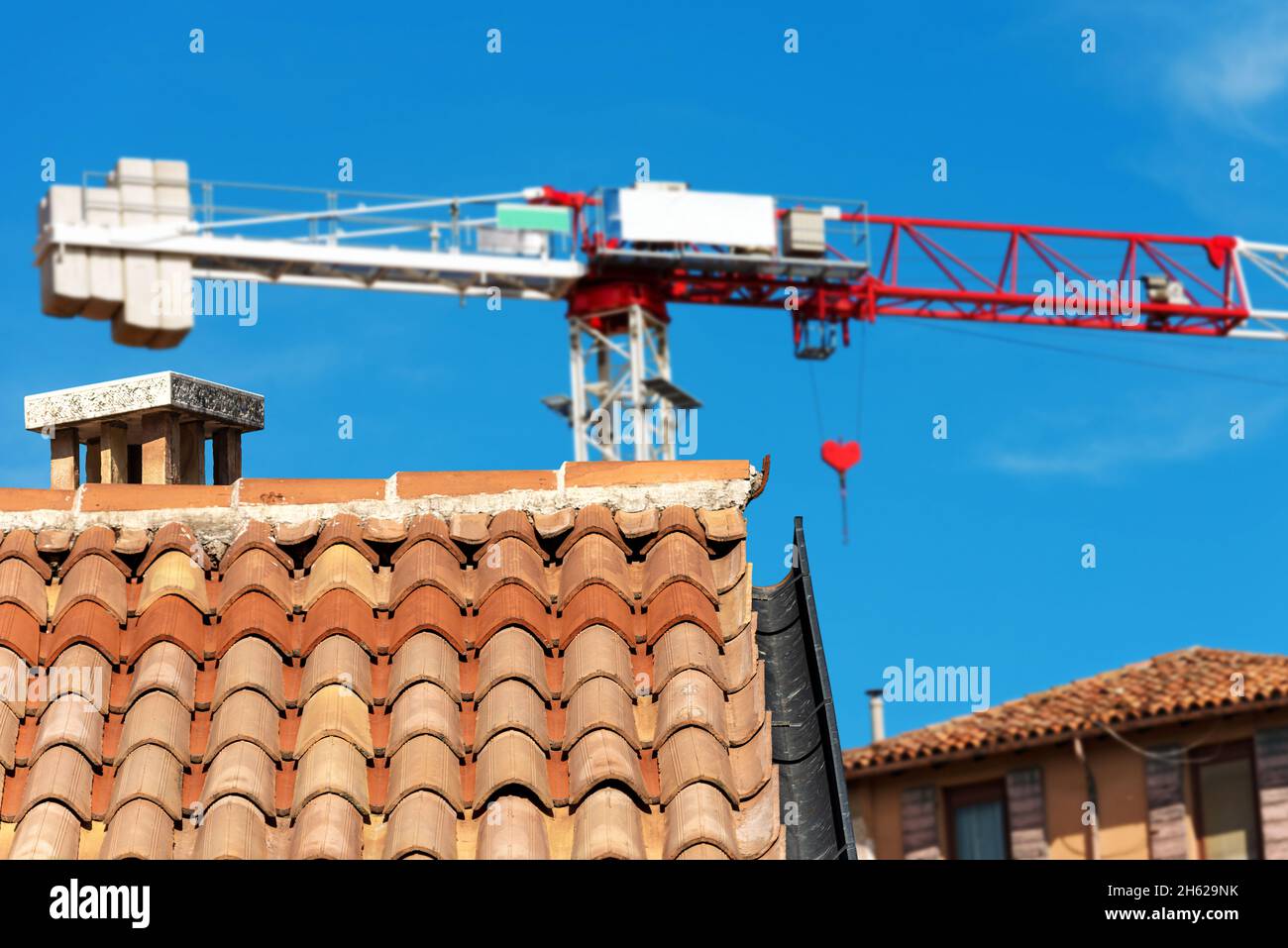 Crane and a closeup of a roof with terracotta tiles (Coppo in Italian) and gutter on a clear sky in a construction site. Construction industry concept Stock Photo