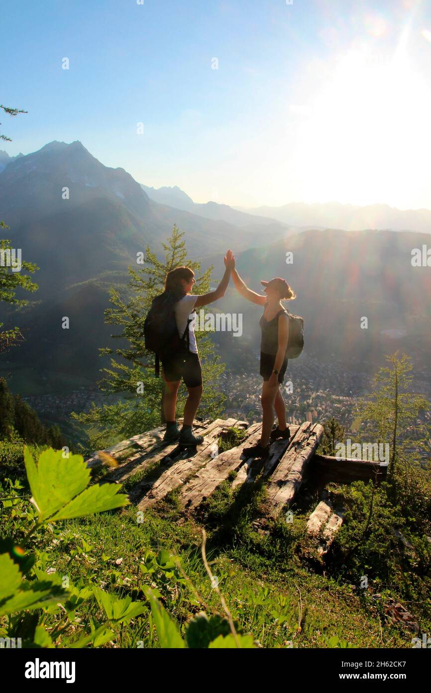 two young women celebrate,rejoice in the backlight,summit happiness,success,clapping,in the background the,wetterstein mountains in sunset,photographed at the mittenwalder hut on the karwendel,mittenwald,upper bavaria,isar valley,bavaria,germany,europe Stock Photo