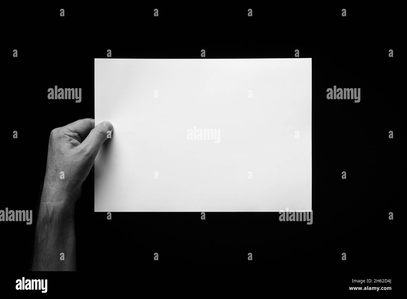 B+W image of male hand holding blank sheet of paper against black ...