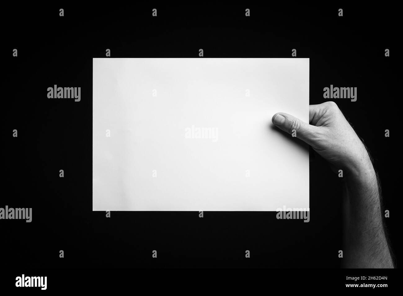 B+W image of male hand holding blank sheet of paper against black ...