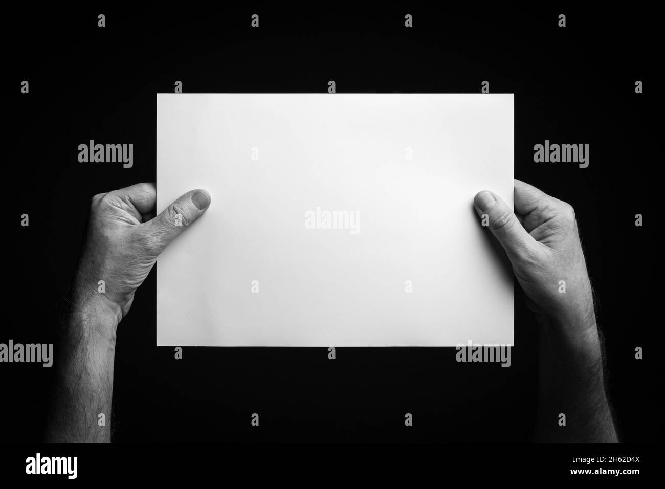 B+W image of male hands holding blank sheet of paper against black ...