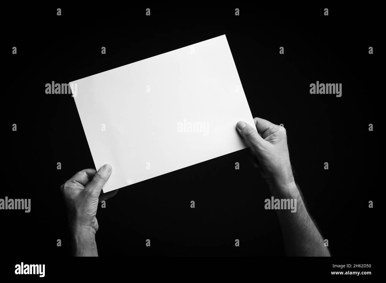 B+W image of male hands holding blank sheet of paper against black ...