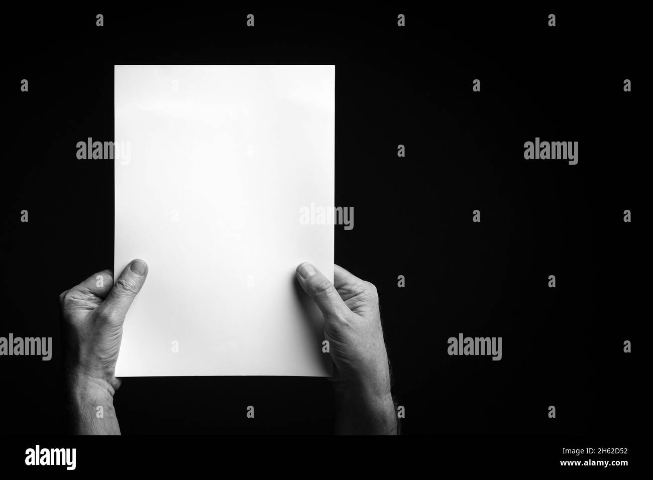 B+W image of male hands holding blank sheet of paper against black ...