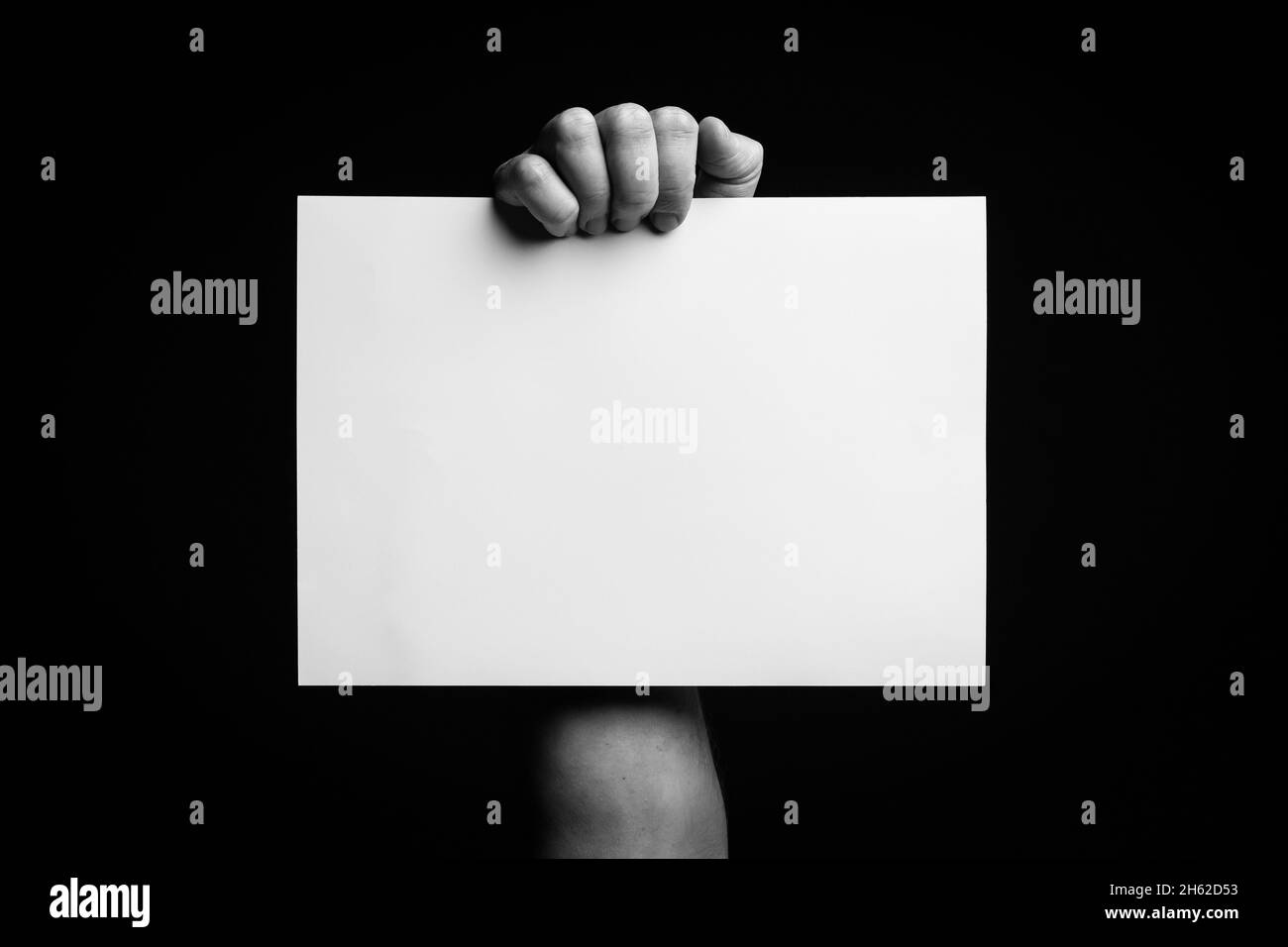 B+W image of male hand holding blank sheet of paper against black ...