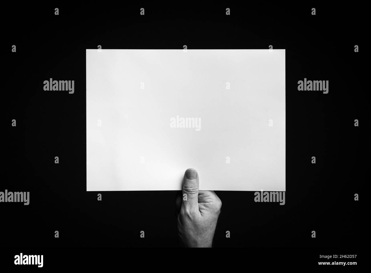 B+W image of male hand holding blank sheet of paper against black ...