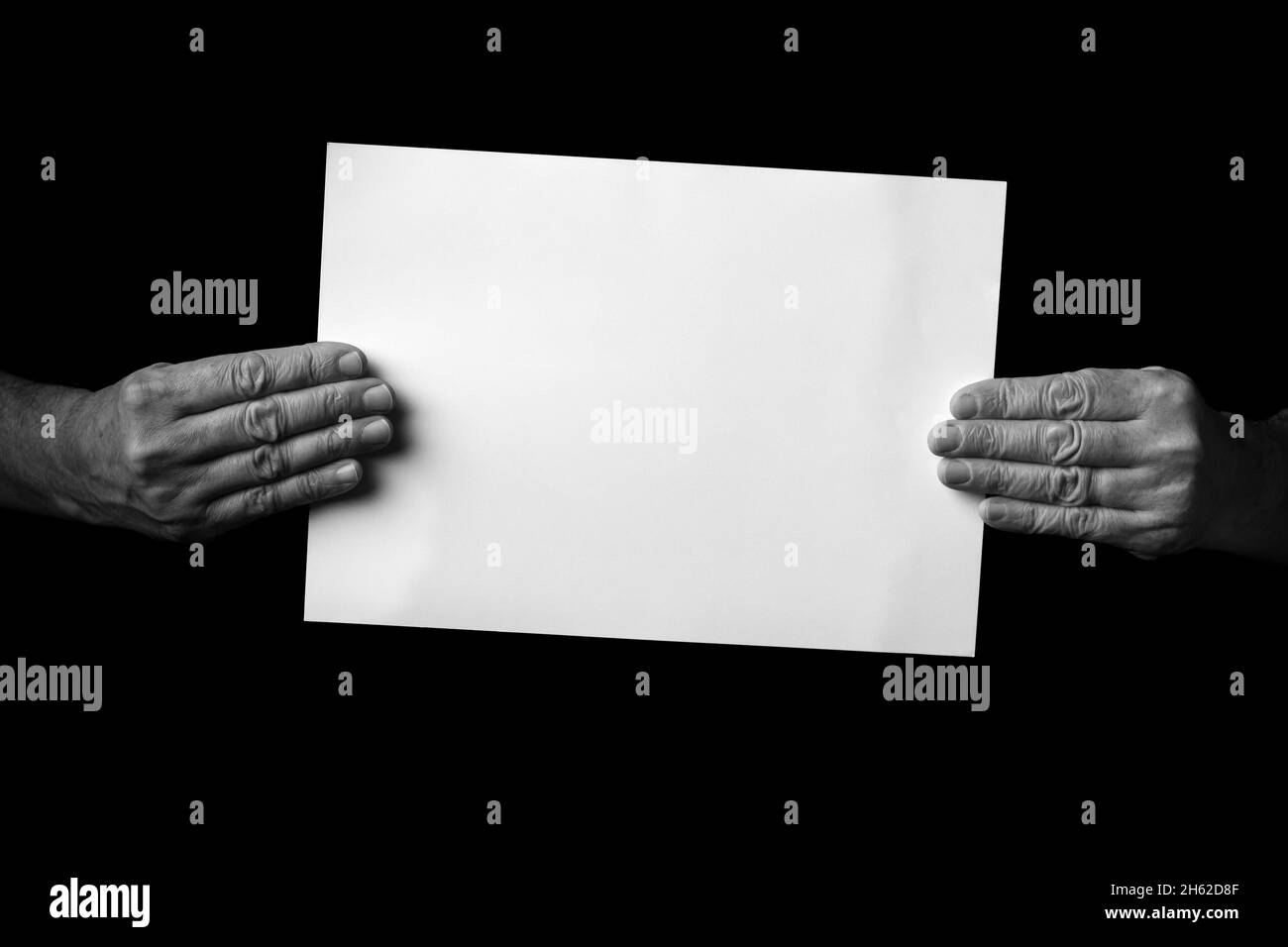B+W image of male hands holding blank sheet of paper against black ...