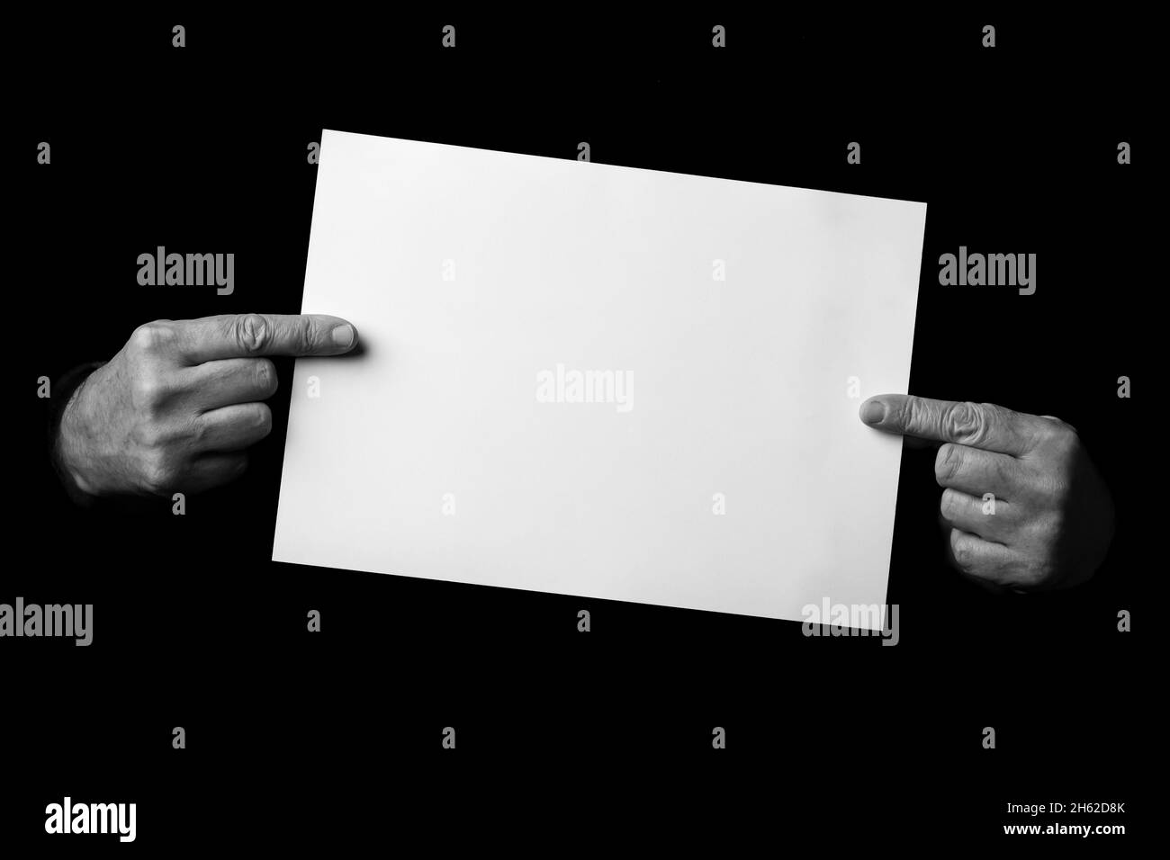 B+W image of male hands holding blank sheet of paper against black ...