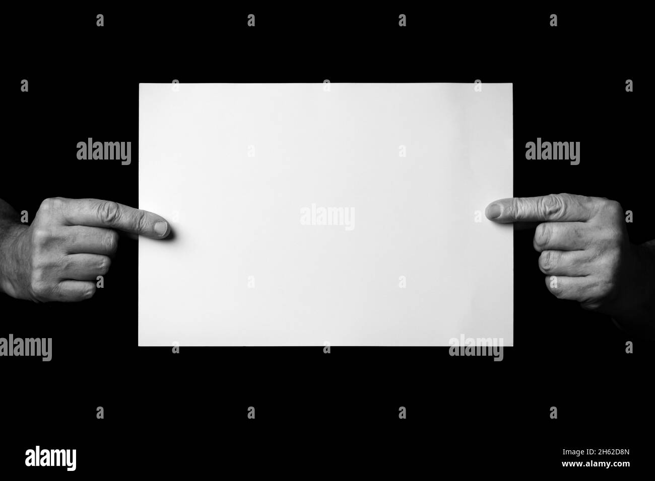 B+W image of male hands holding blank sheet of paper against black ...