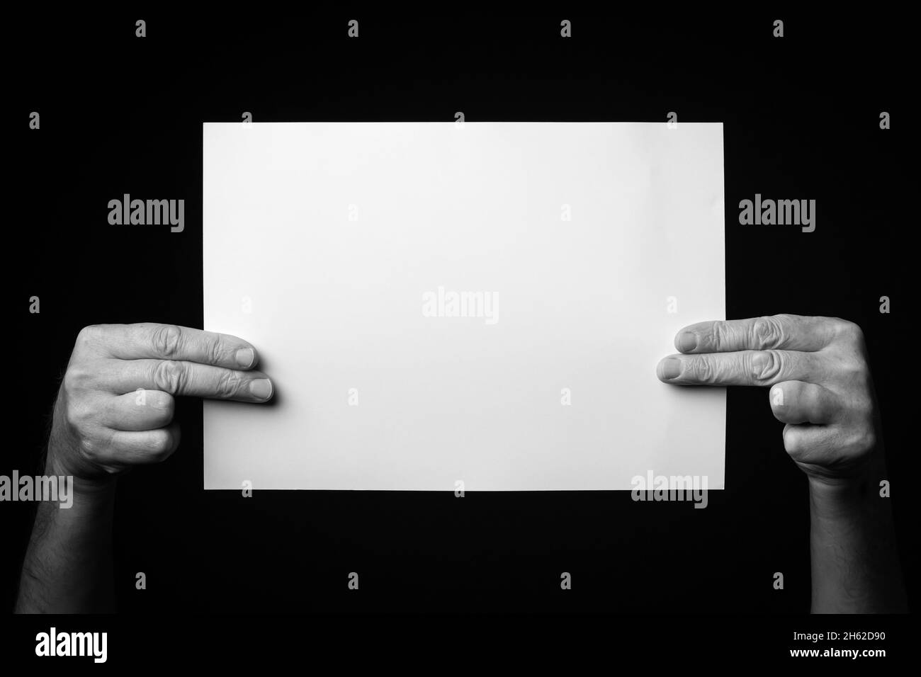 B+W image of male hands holding blank sheet of paper against black ...