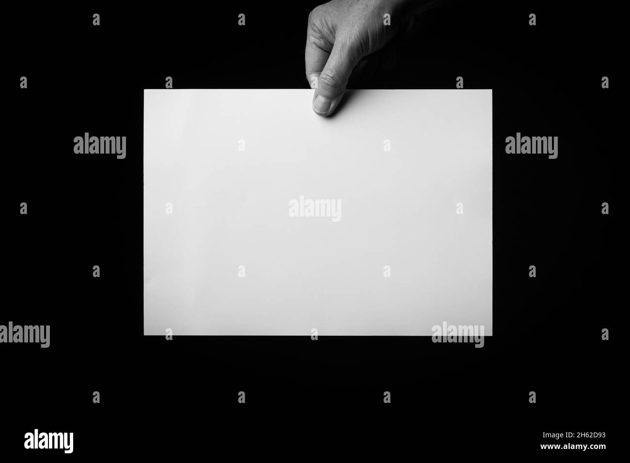B+W image of male hand holding blank sheet of paper against black ...