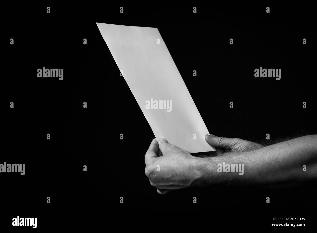 B+W image of male hands holding blank sheet of paper against black ...
