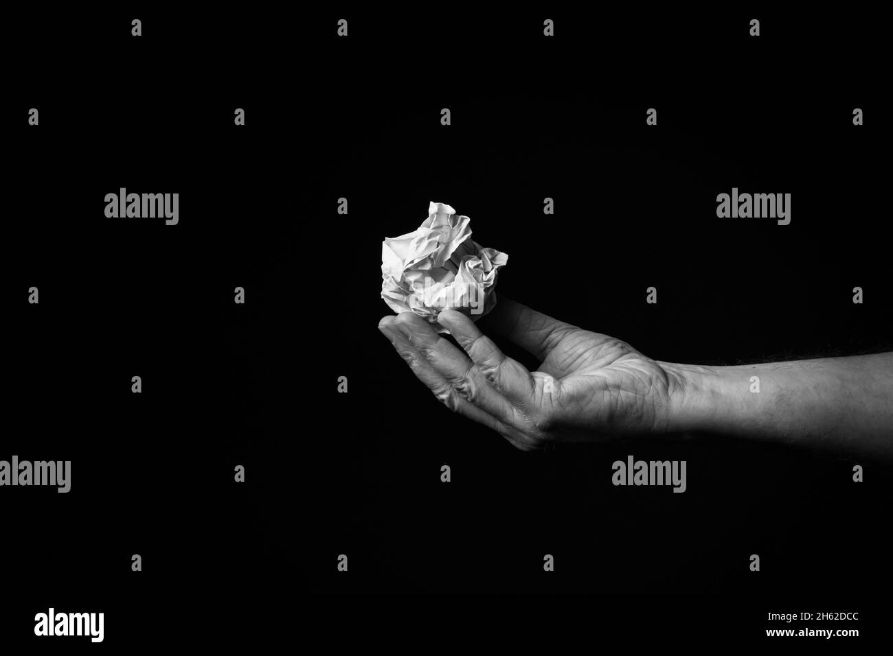 B+W image of male hand holding crumpled ball of paper against black